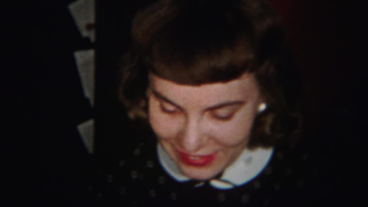 Young woman in a dark polka dot dress looks downward and smiles indoors.