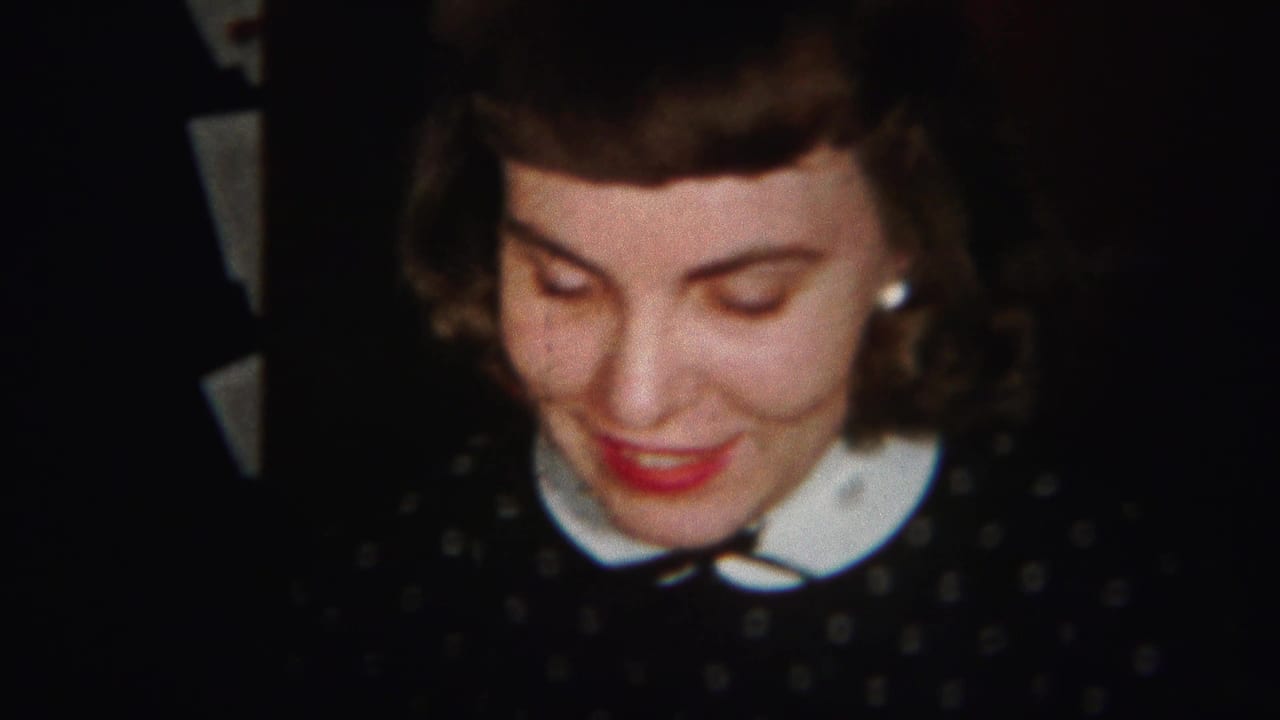 Young woman smiles with her eyes lowered against a dark indoor background.