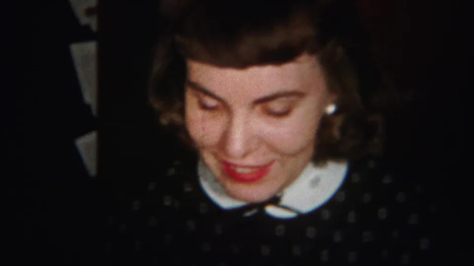 The young woman remains in close view, smiling with lowered eyes, her white collar and red lipstick visible in the 1951 home-movie frame.