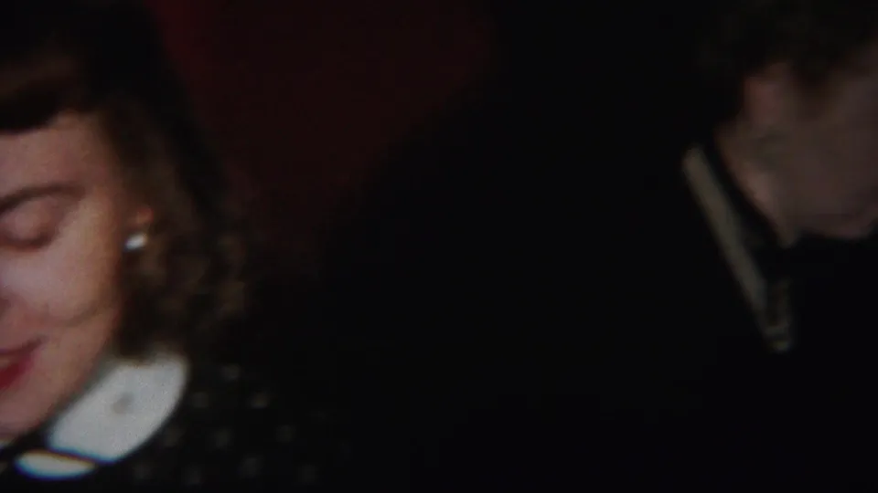 The young woman's face is partly cropped at the left edge, with her white collar and dark dress still visible in the dim indoor scene.