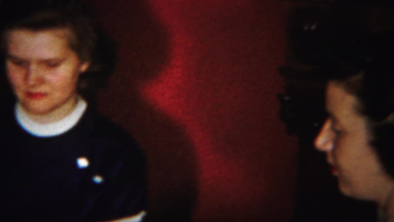 Young woman in a dark sweater seated against a red wall.