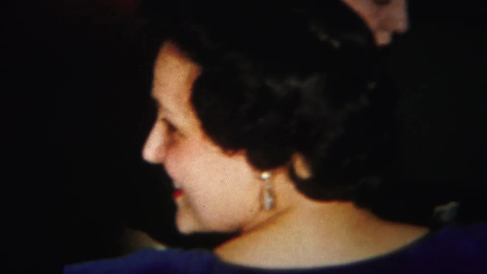 A woman with styled dark hair and pearl earrings appears in profile during the 1951 indoor card-game scene.