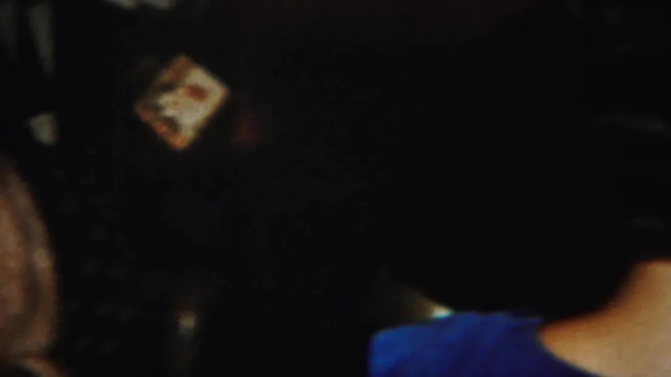 A close, underexposed view shows women around the card table, with a hand holding playing cards visible in the center.