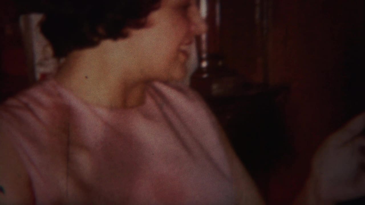 Woman turns to the side in a wood-paneled home interior, with another person partly visible at right.