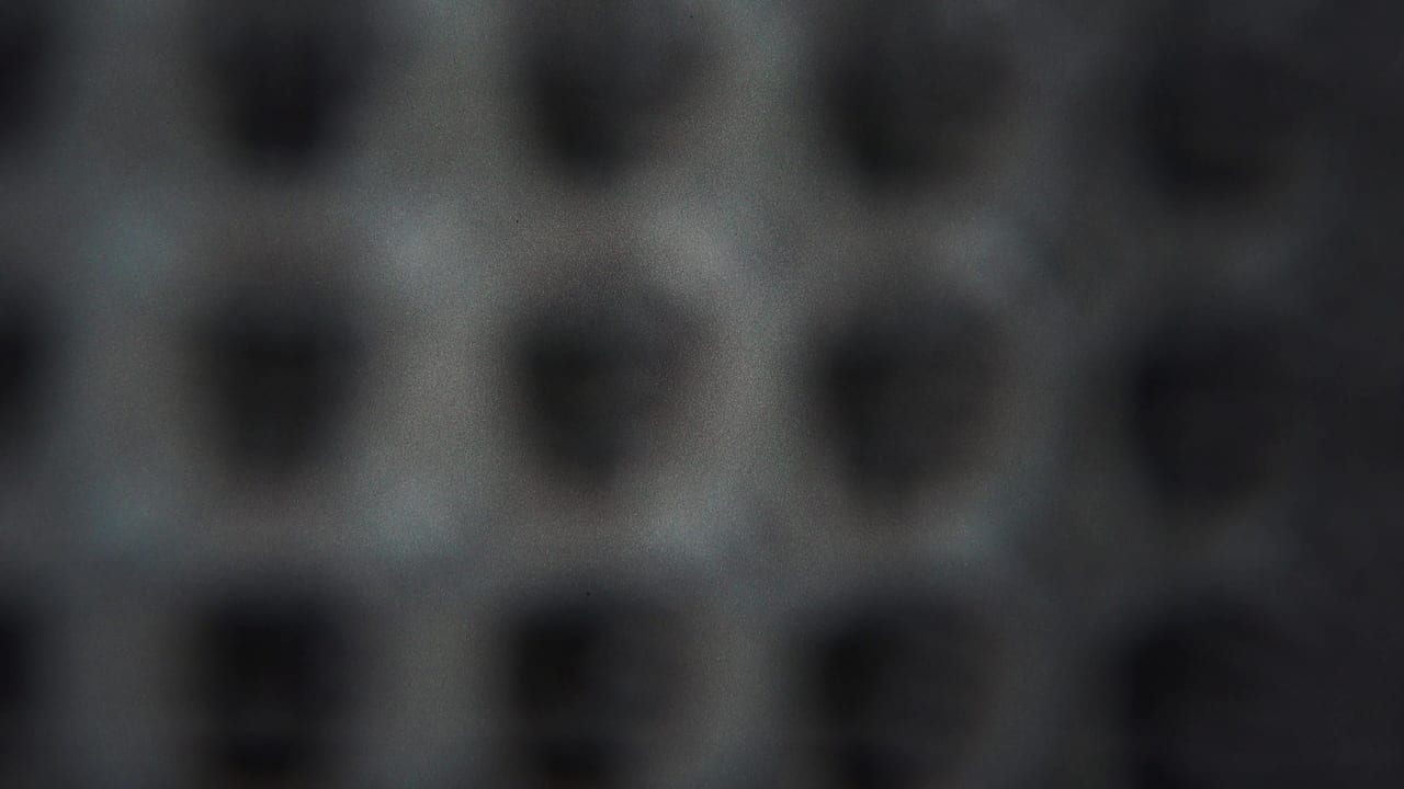 Blurred repeating dark shapes on a pale textured background.
