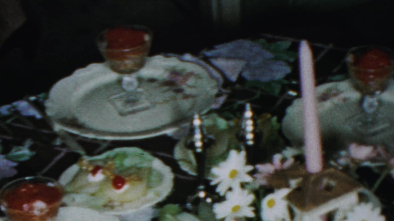 1959 Paramus dinner table view with white dishes, glass dessert cups, a tall pink candle, daisies, and a dessert topped with cherries.