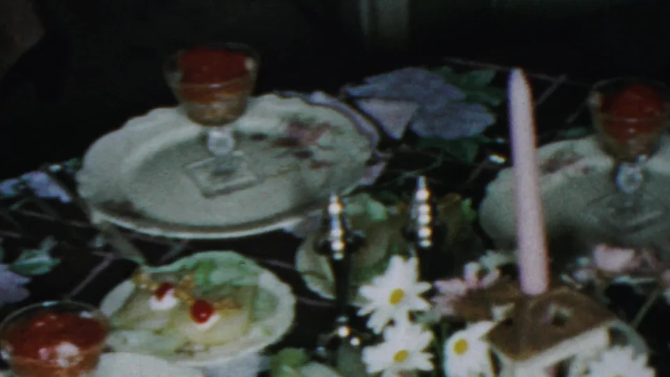 1959 Paramus dinner table view with white dishes, glass dessert cups, a tall pink candle, daisies, and a dessert topped with cherries.