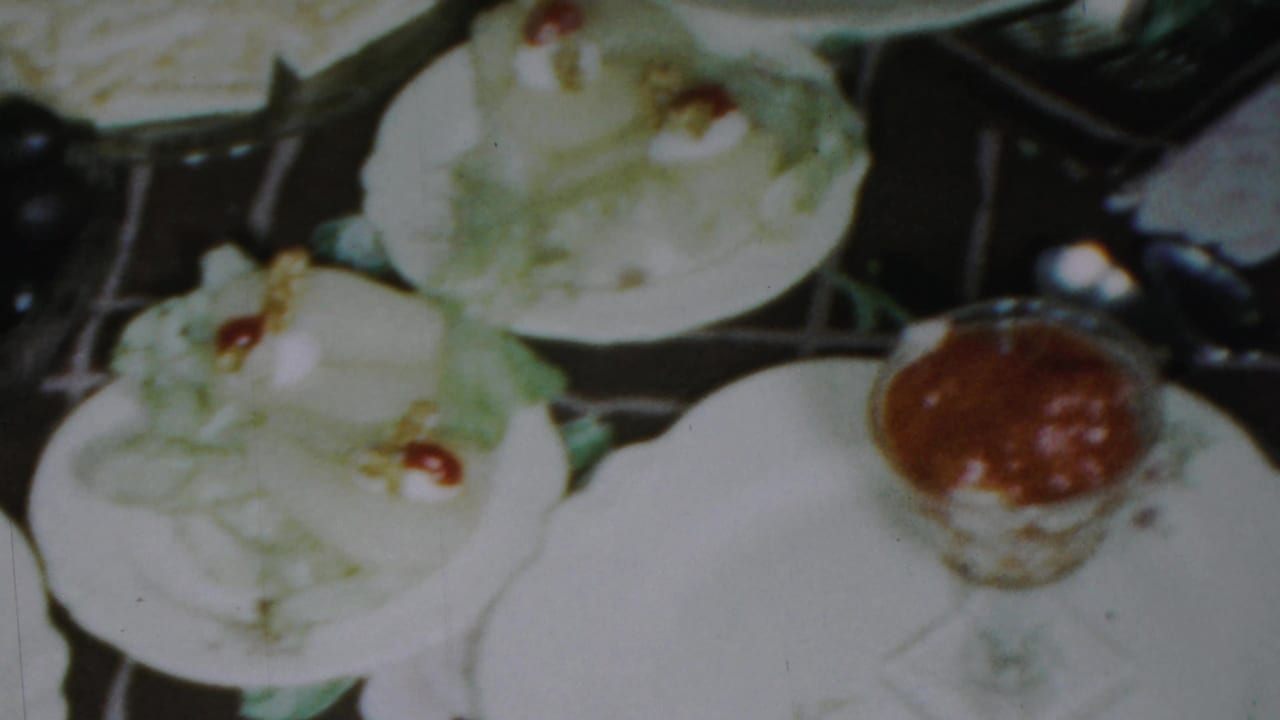 Close-up of the holiday table in Paramus, New Jersey, with pale desserts, floral plates, and a small glass cup of red sauce visible in 8mm color.