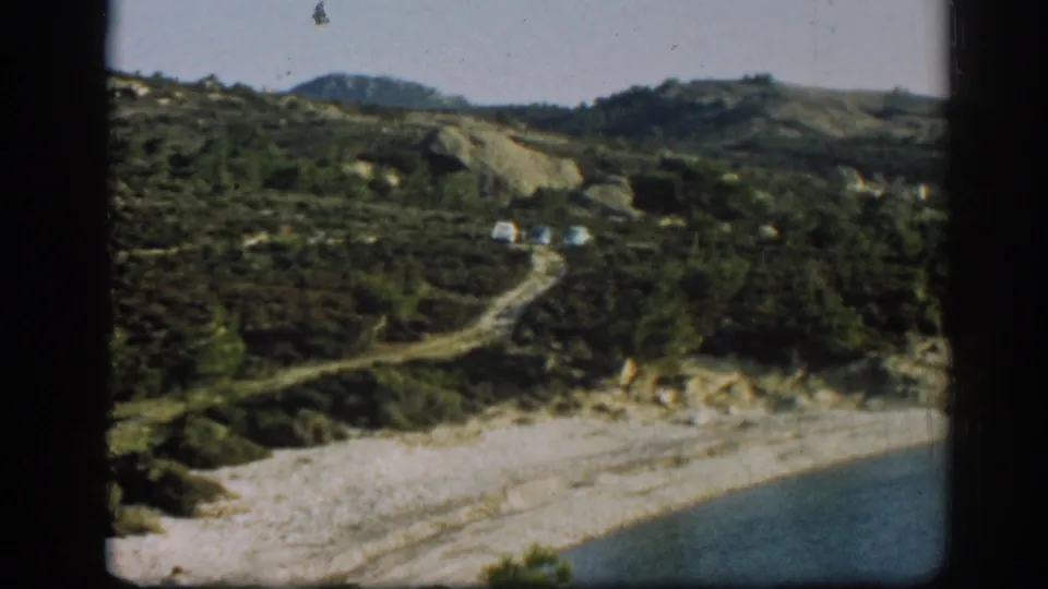 1962 home-movie view near Ephesus, Turkey, with three cars on a dirt mountain road above a shoreline.