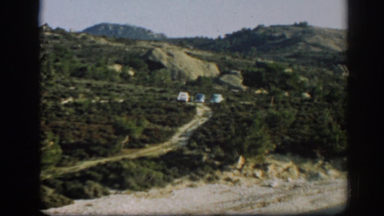 Dirt road curves through green hills toward three small parked cars.