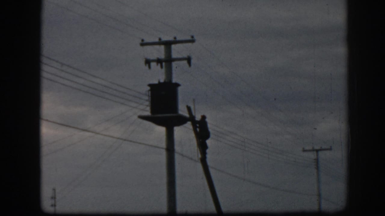 In Ephesus, Turkey, 1962, a silhouetted utility worker climbs a ladder beside a transformer and overhead wires.