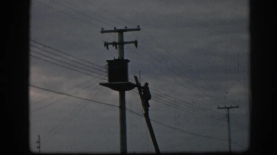 In Ephesus, Turkey, 1962, a silhouetted utility worker climbs a ladder beside a transformer and overhead wires.