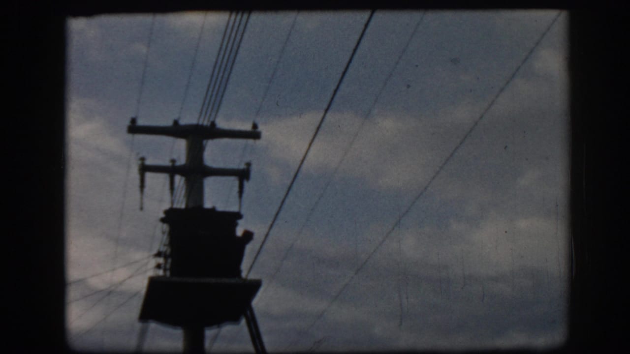 Silhouetted utility pole and overhead power lines against a cloudy sky.