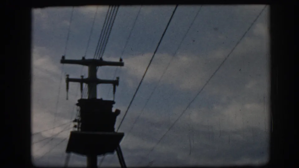 1962 Ephesus 8mm frame showing a dark utility pole, crossarms, insulators, and power lines under a cloudy sky.