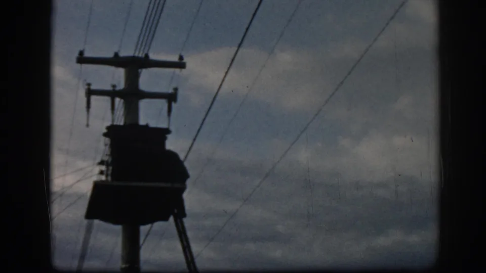 1962 Ephesus frame with a silhouetted utility pole, diagonal power lines, and muted cloudy sky on 8mm film.