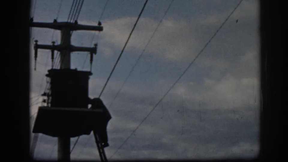 1962 Ephesus 8mm still showing the utility pole structure larger in frame, with overhead lines and cloudy sky.
