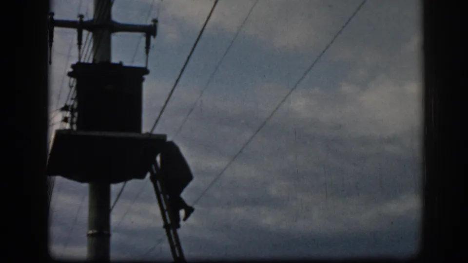 1962 Ephesus frame showing a silhouetted pole, attached structure, and overhead wires in a cloudy sky.