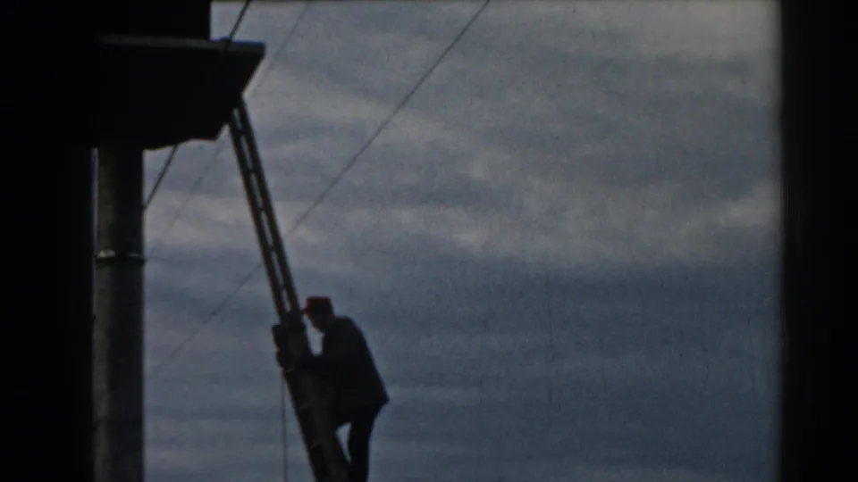 Near the end of the clip, the worker is almost down the ladder beside the utility pole, framed by wires and cloudy sky.