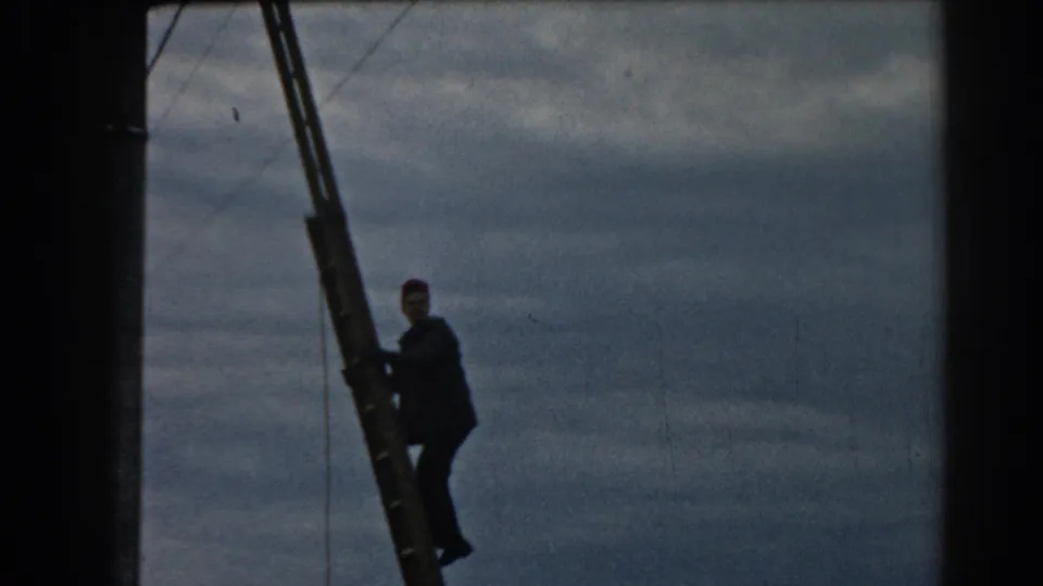 In the 1962 Turkey footage, the worker appears partway up the ladder, silhouetted against a clouded sky with wires nearby.