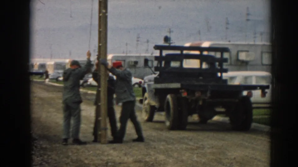 Three men in work clothes, including one wearing a red cap, reposition a wooden pole at a roadside location in Ephesus, Turkey, according to the clip metadata.