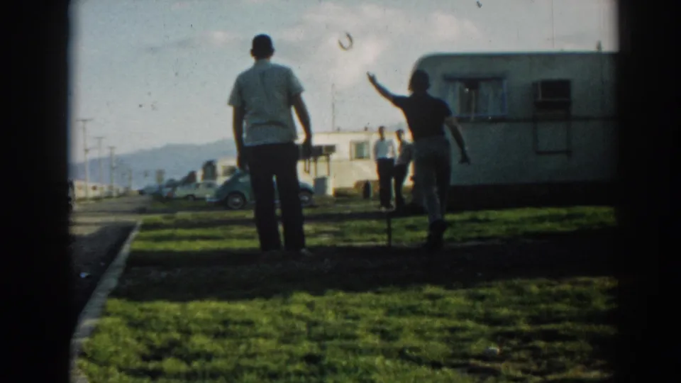 At the 1962 Ephesus camper site, one man appears to toss a horseshoe as another stands nearby on the grass.