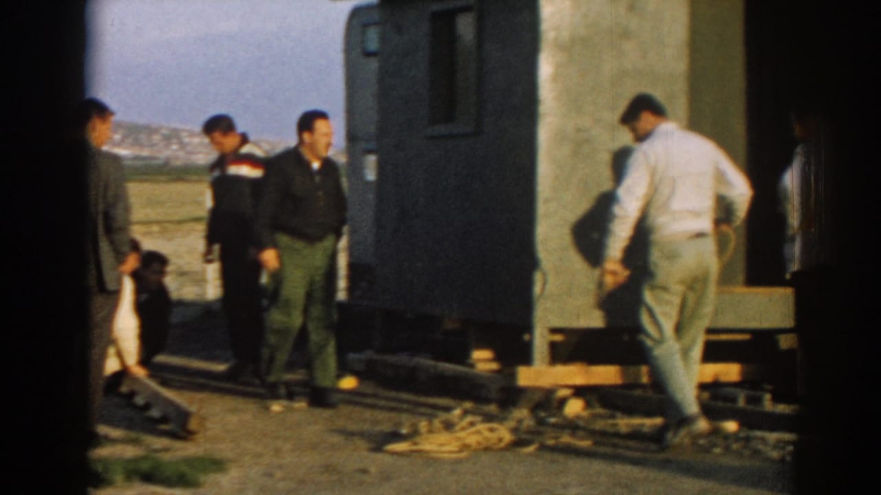 Men stand and handle rope beside a portable structure in open daylight.