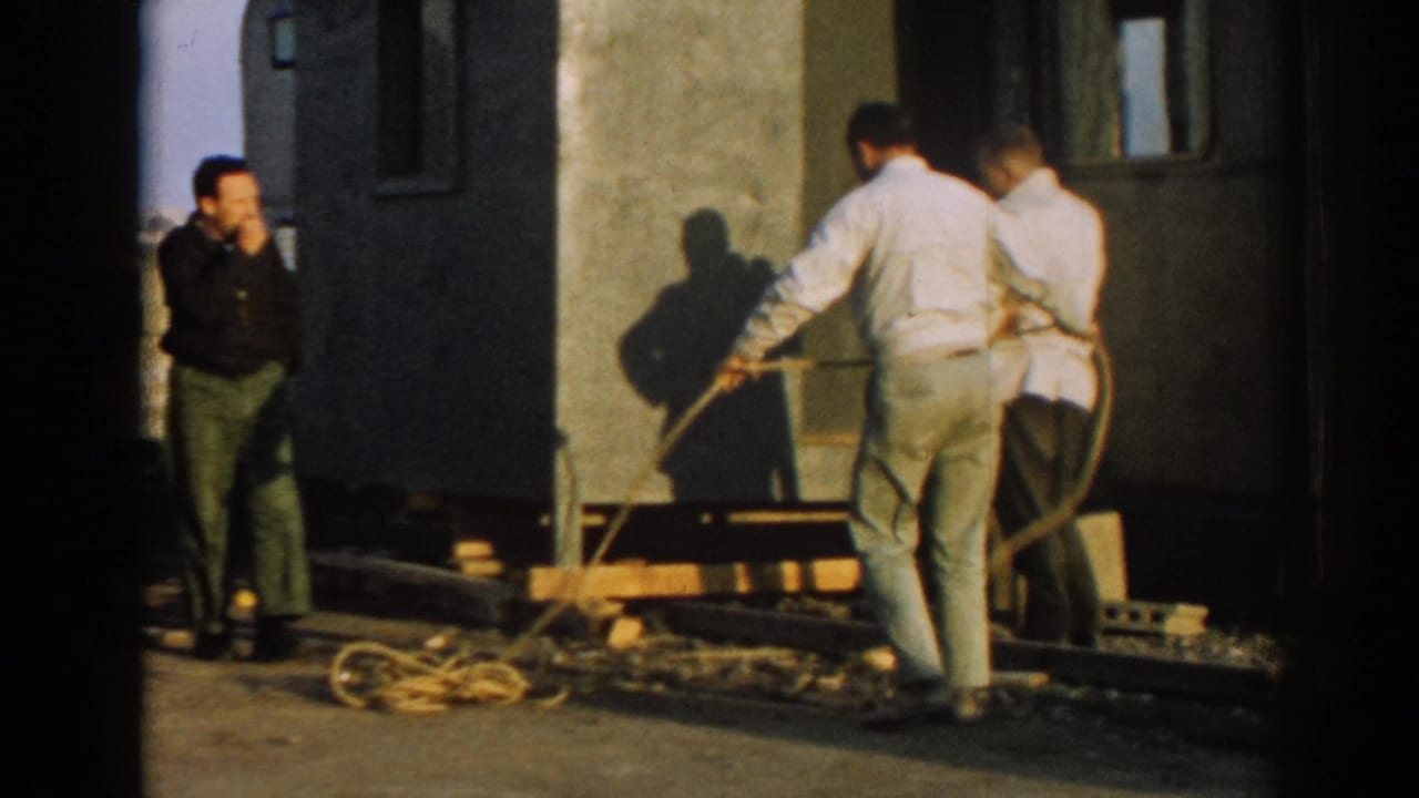 Two men work with a long rope beside a dark doorway and raised structure.