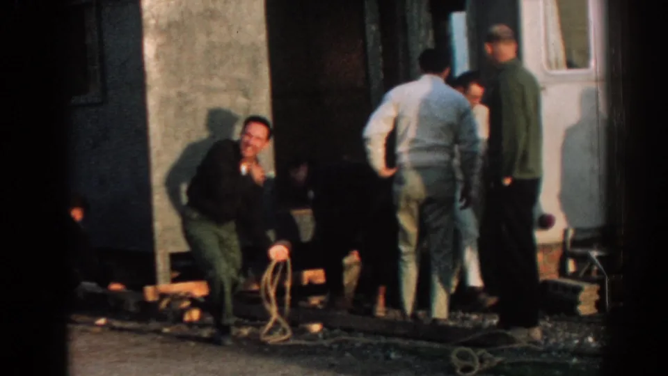 A group of adult men in 1962 Ephesus gather around rope and supports beside a structure, with one man crouched low.