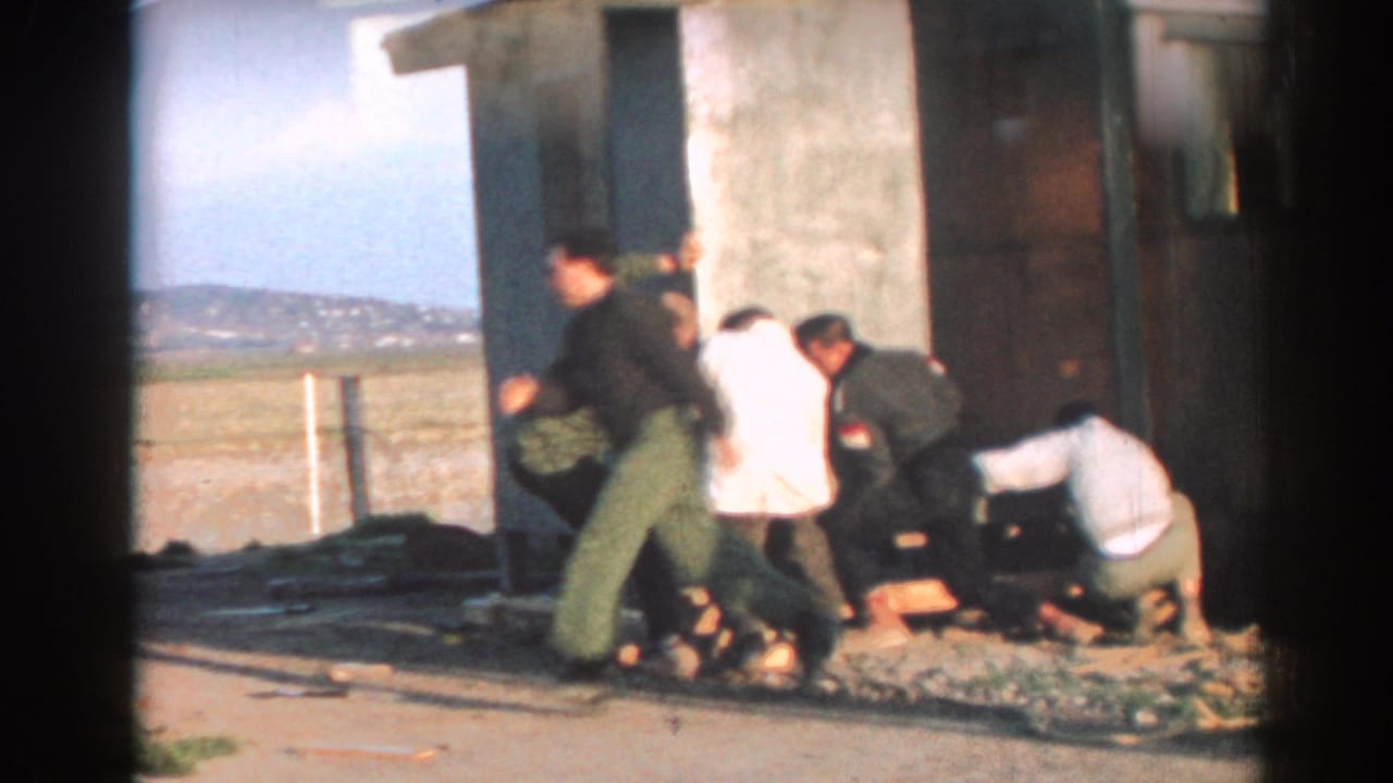 Men gather beside a small building while one man moves quickly past the work area.