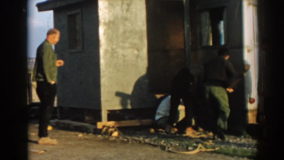 In 1962 Ephesus, Turkey, several men work beside a small site structure as a man in a green jacket observes nearby.