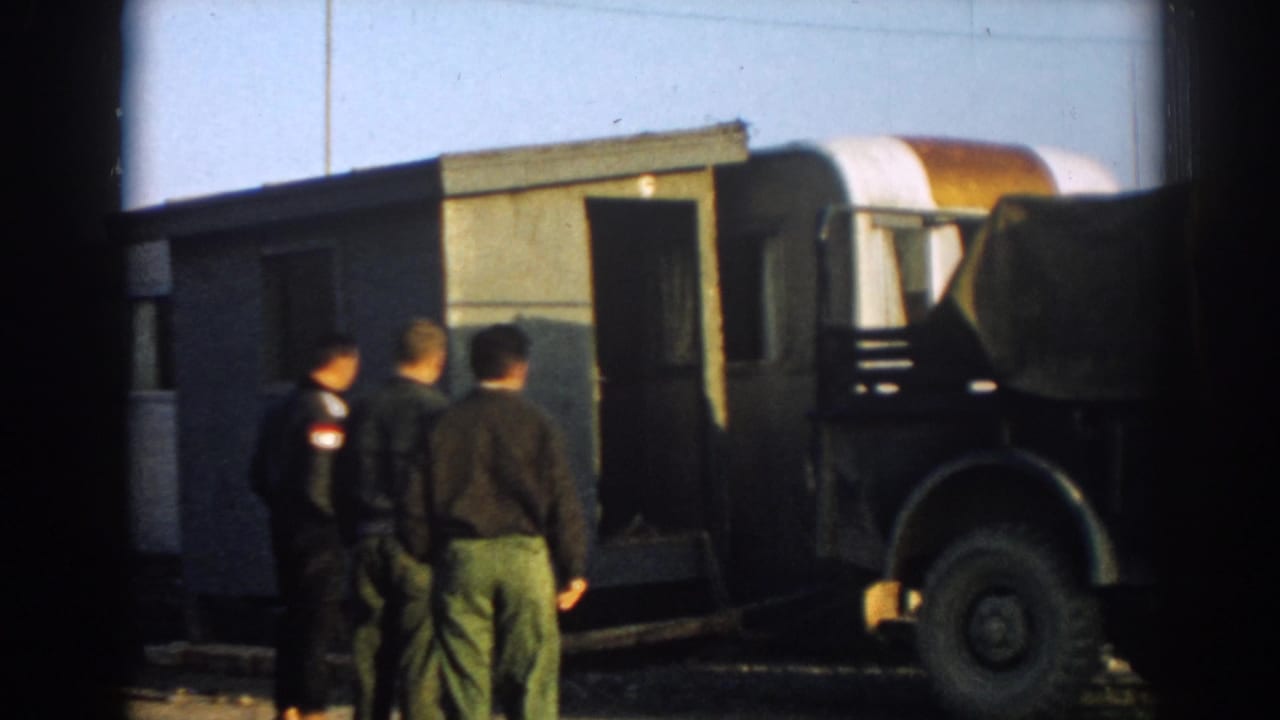Three men walk toward a small site structure beside a canvas-covered military-style truck in 1962 Ephesus, Turkey.