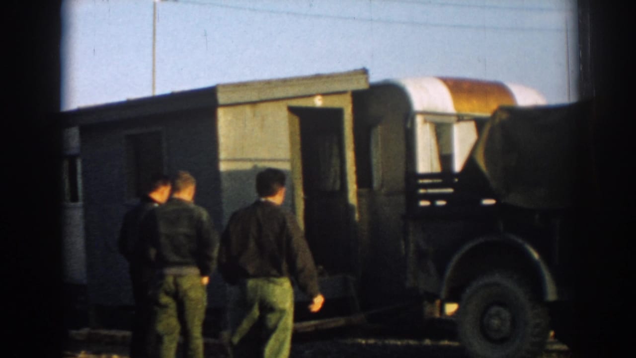Several men move around a small structure and canvas-covered military-style truck at an outdoor site in 1962 Ephesus, Turkey.