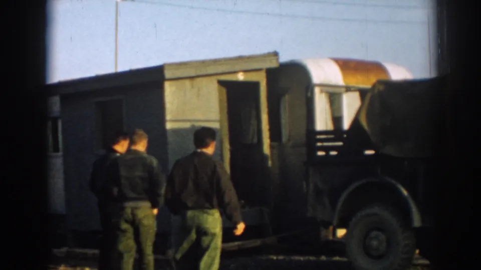 Several men move around a small structure and canvas-covered military-style truck at an outdoor site in 1962 Ephesus, Turkey.