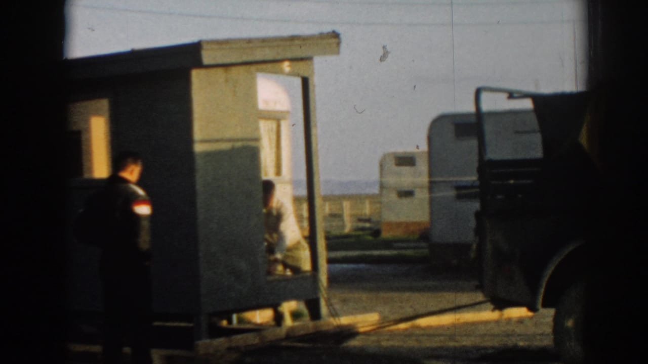 Uniformed man beside a small shelter with a caravan trailer in the background.