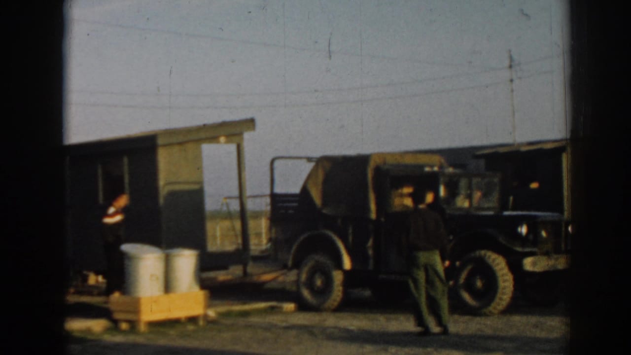 A parked military truck fills the foreground while men stand near a small shelter at the Ephesus camp.