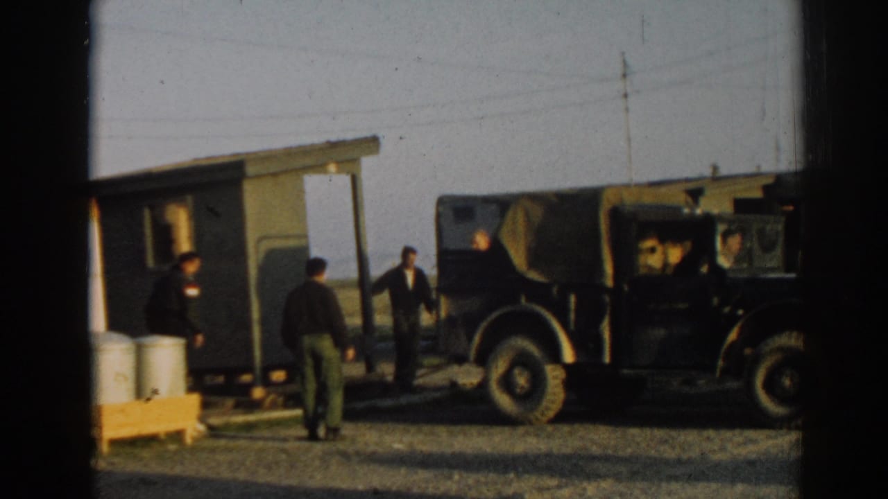 1962 Ephesus, Turkey frame showing several men near a small green wooden structure, a canvas-topped jeep, and metal drums.