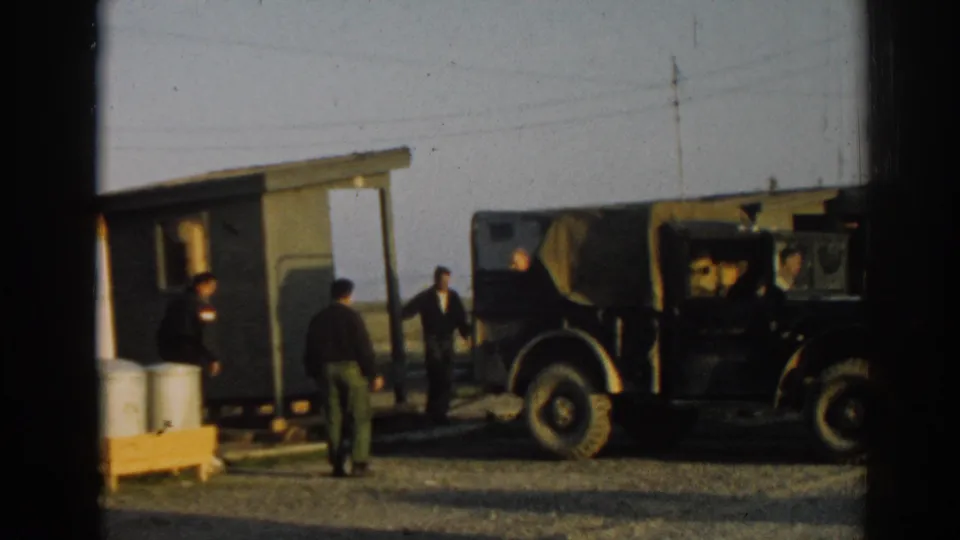 1962 Ephesus, Turkey frame showing several men near a small green wooden structure, a canvas-topped jeep, and metal drums.