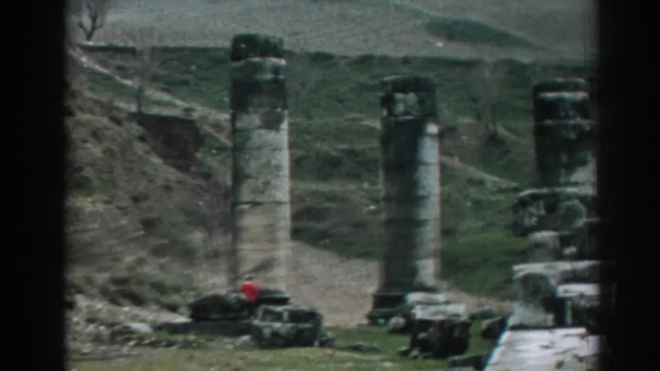 1962 8mm view of Ephesus, Turkey, showing weathered columns, scattered stonework, and a red-jacketed visitor near the base of the ruins.