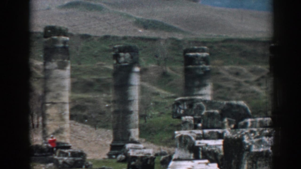 Ephesus ruin site on 1962 color 8mm film, with tall columns, stone blocks, hillside paths, and a small red-clad visitor at left.