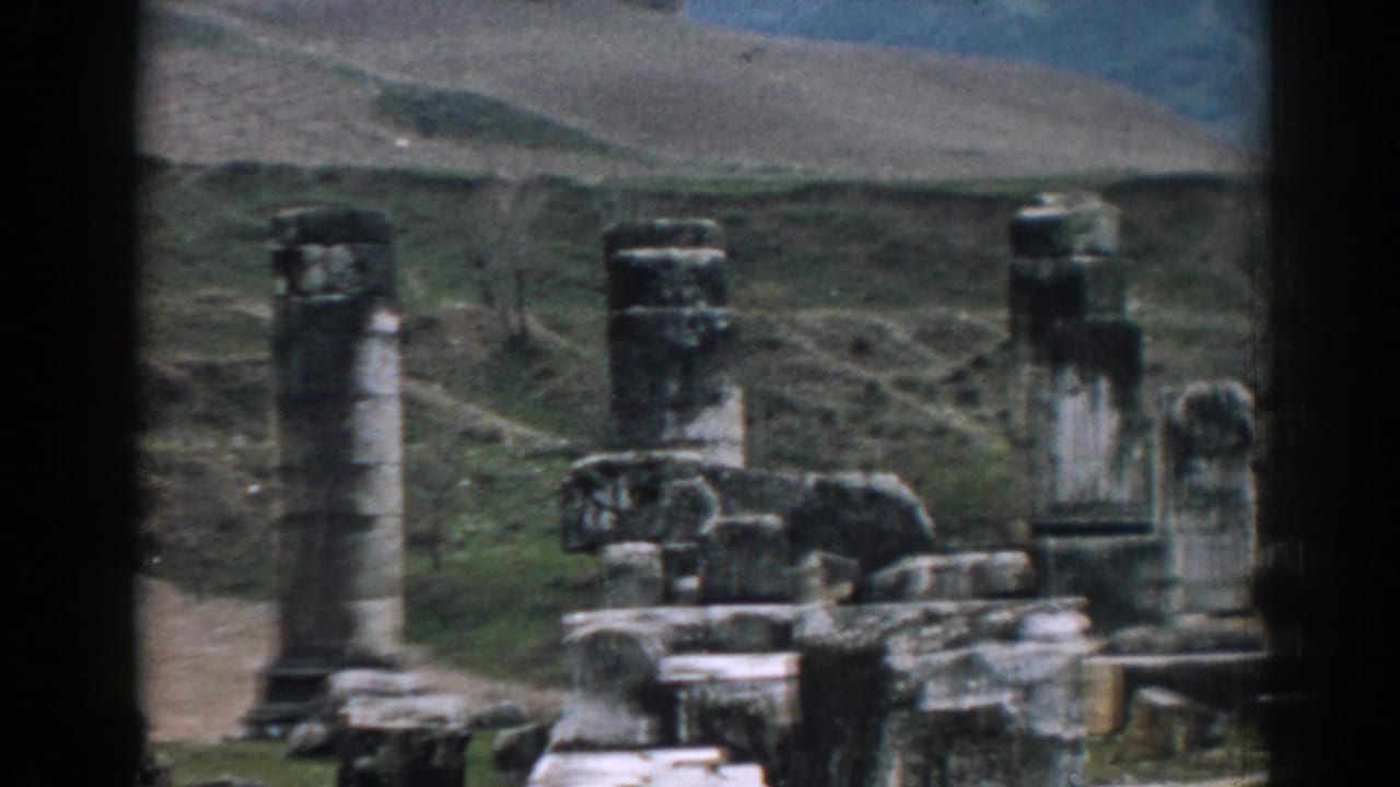 1962 Ephesus home-movie frame showing a closer cluster of weathered columns and carved stone rubble against green and tan hills.