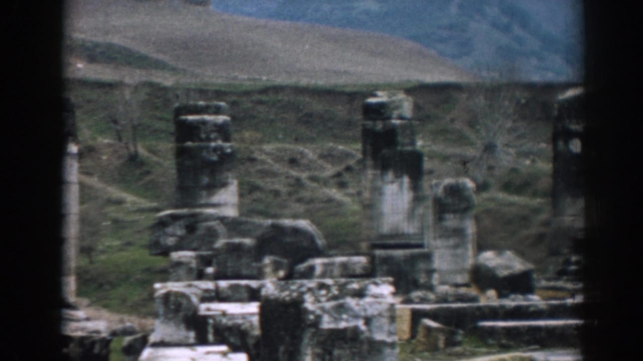 Late frame from the 1962 Ephesus 8mm clip, showing tall grey columns, scattered ancient stonework, and rolling hills behind the ruin site.