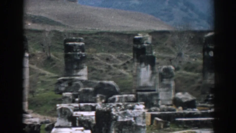 Late frame from the 1962 Ephesus 8mm clip, showing tall grey columns, scattered ancient stonework, and rolling hills behind the ruin site.