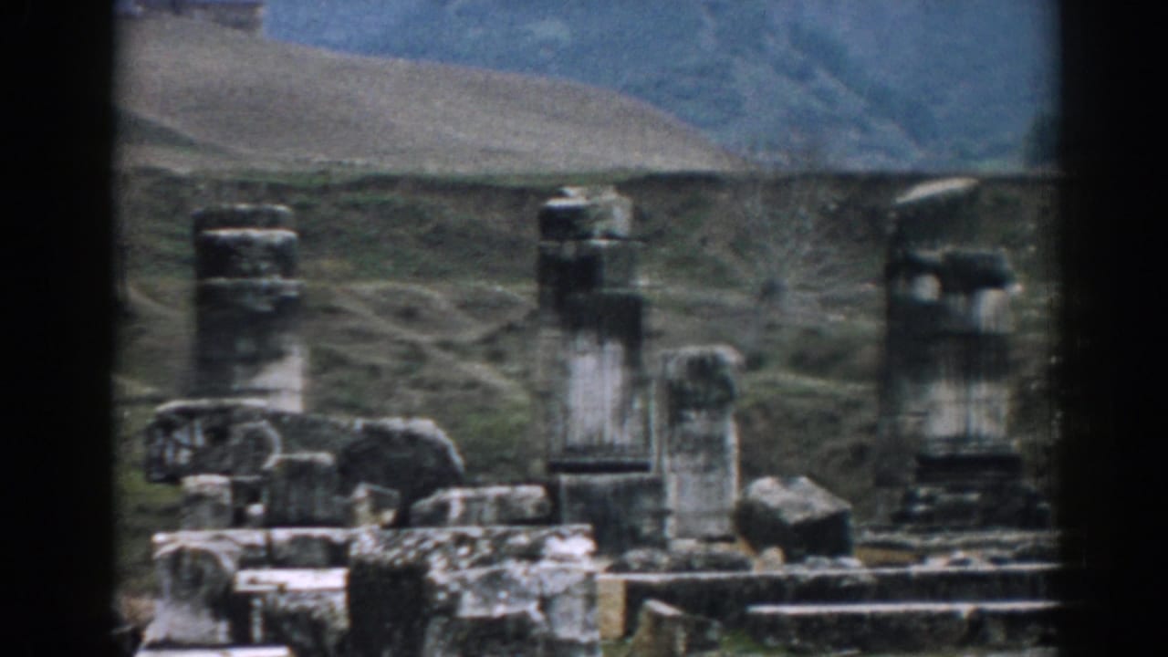 Weathered stone columns and ruin fragments set against hills.