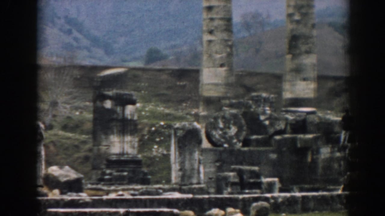 1962 Ephesus view with a vertical column, scattered ancient masonry, sparse plants, and hills behind the site.