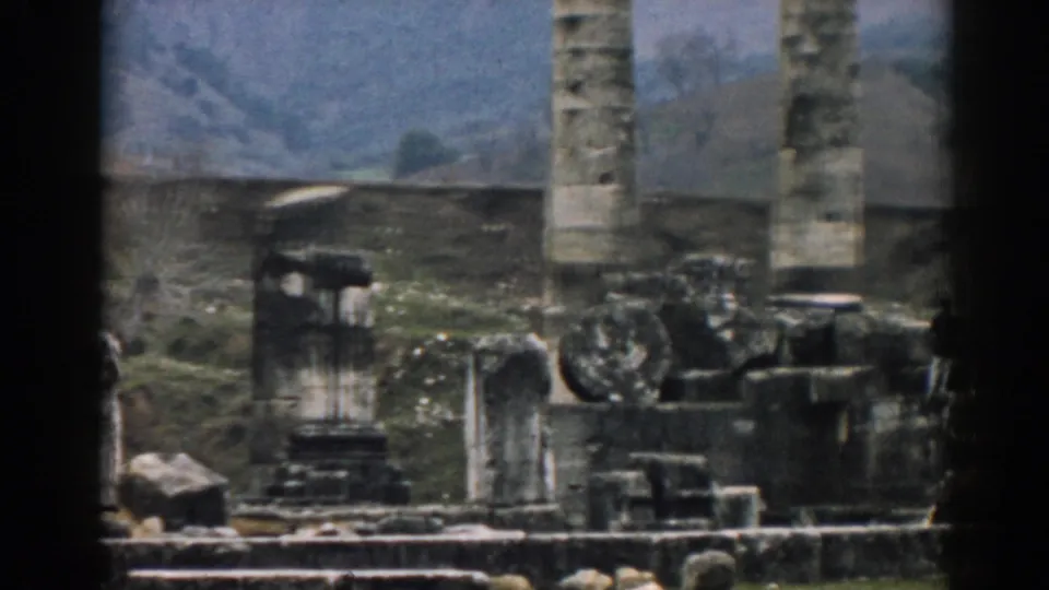 1962 Ephesus view with a vertical column, scattered ancient masonry, sparse plants, and hills behind the site.