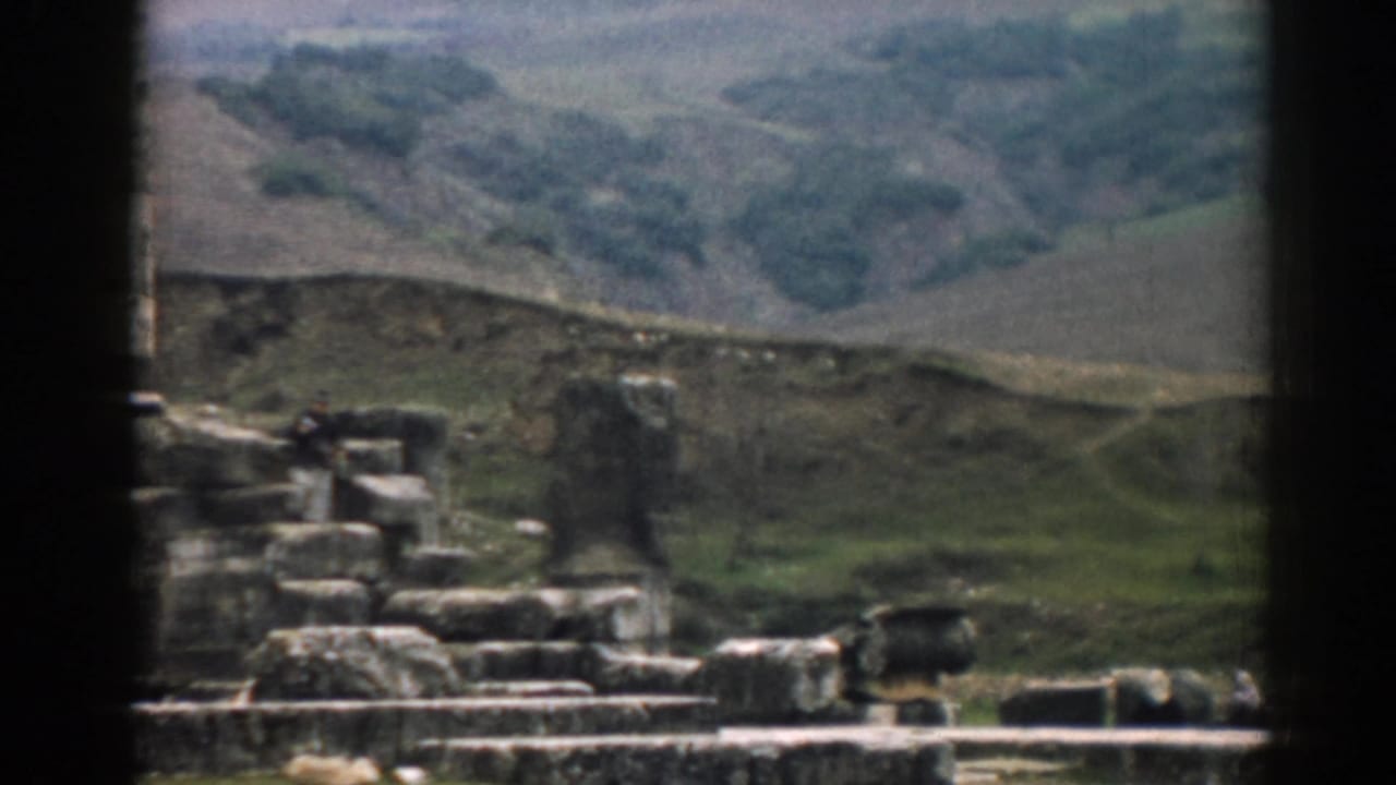 Ancient stone ruins and a small adult figure near steps, with hills in the background.