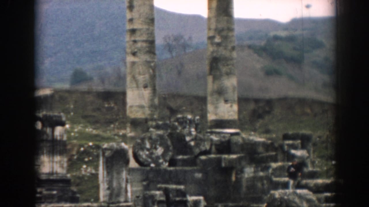 1962 Ephesus home-movie frame showing columns, rubble, and a distant adult visitor among the ruins.