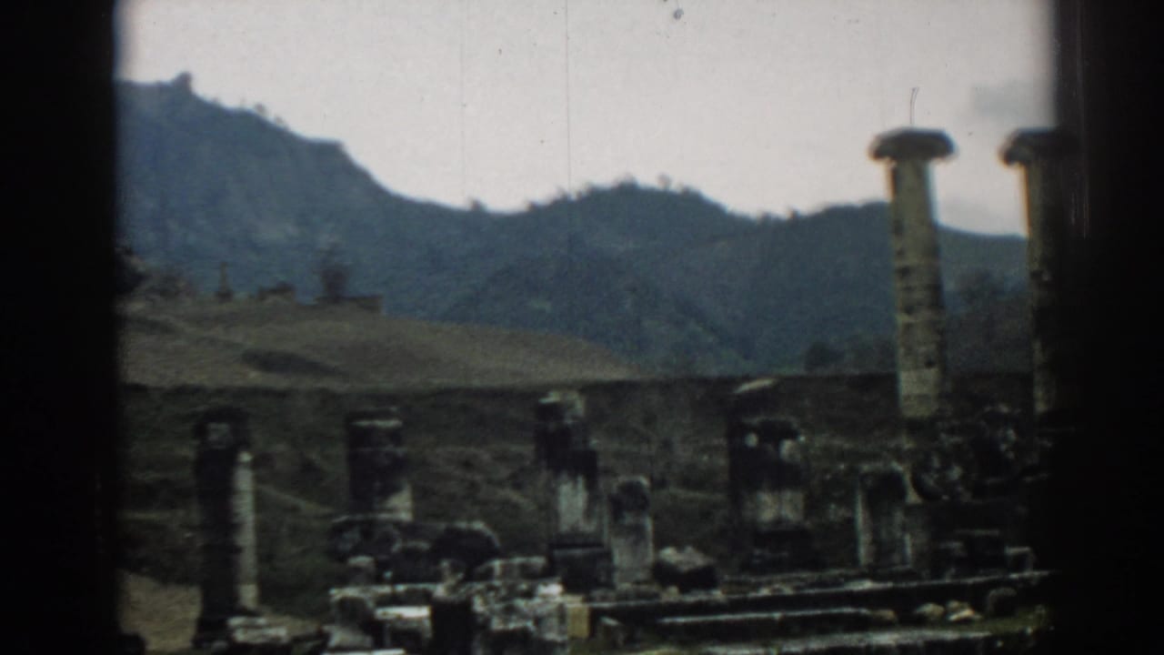 1962 Ephesus travel footage frame with a partial tall column at right, low stone remains across the foreground, and hills behind.