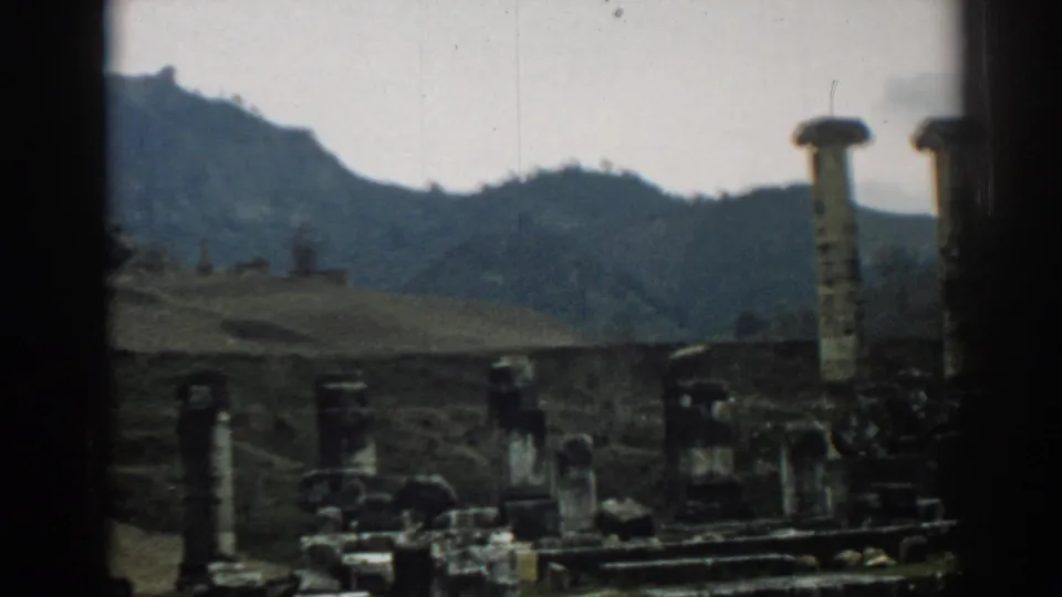 1962 Ephesus travel footage frame with a partial tall column at right, low stone remains across the foreground, and hills behind.