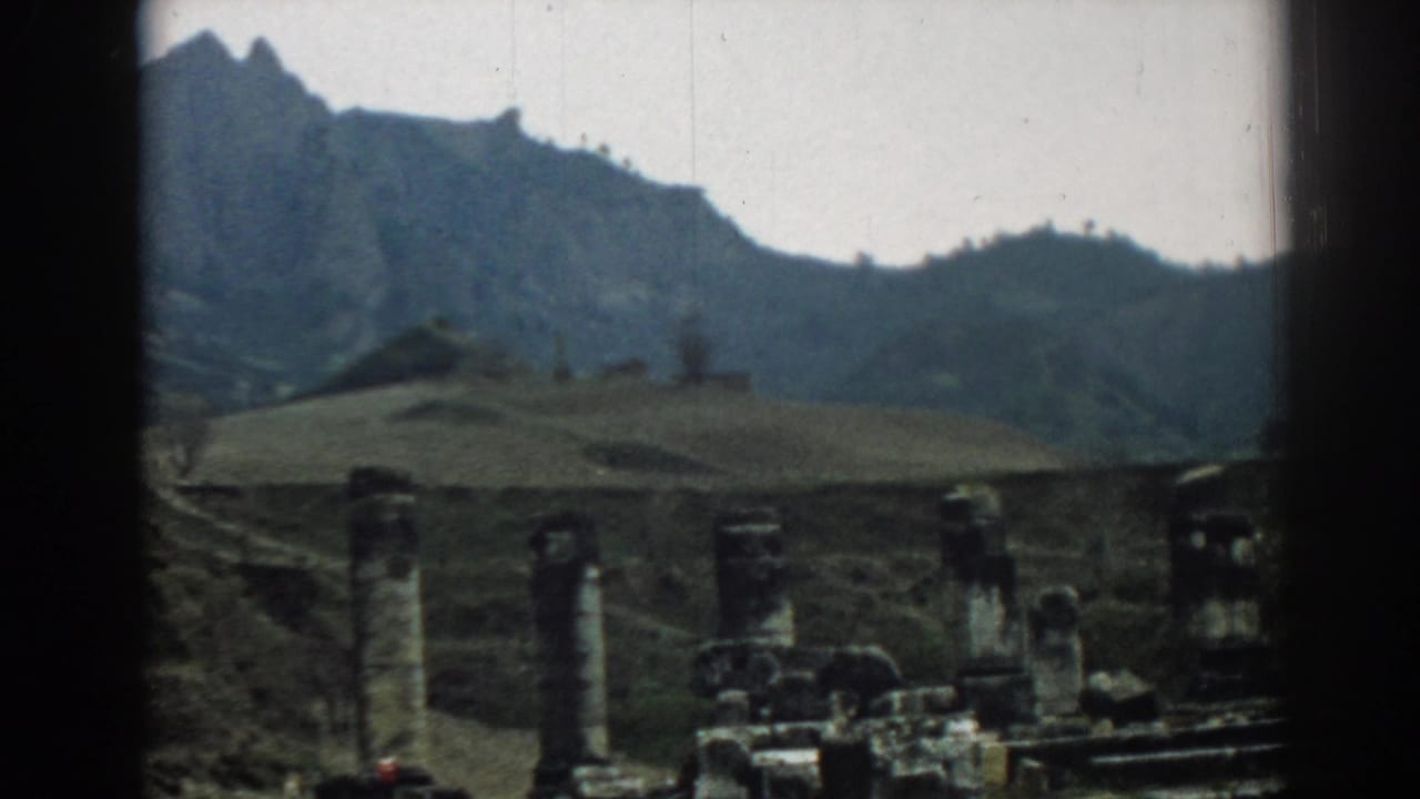 1962 8mm view at Ephesus, Turkey, with weathered columns, low ruins, hills, and a rugged mountain under a pale sky.